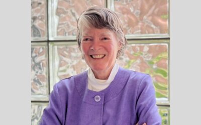 Susan Almy smiling in front of a glass block window.