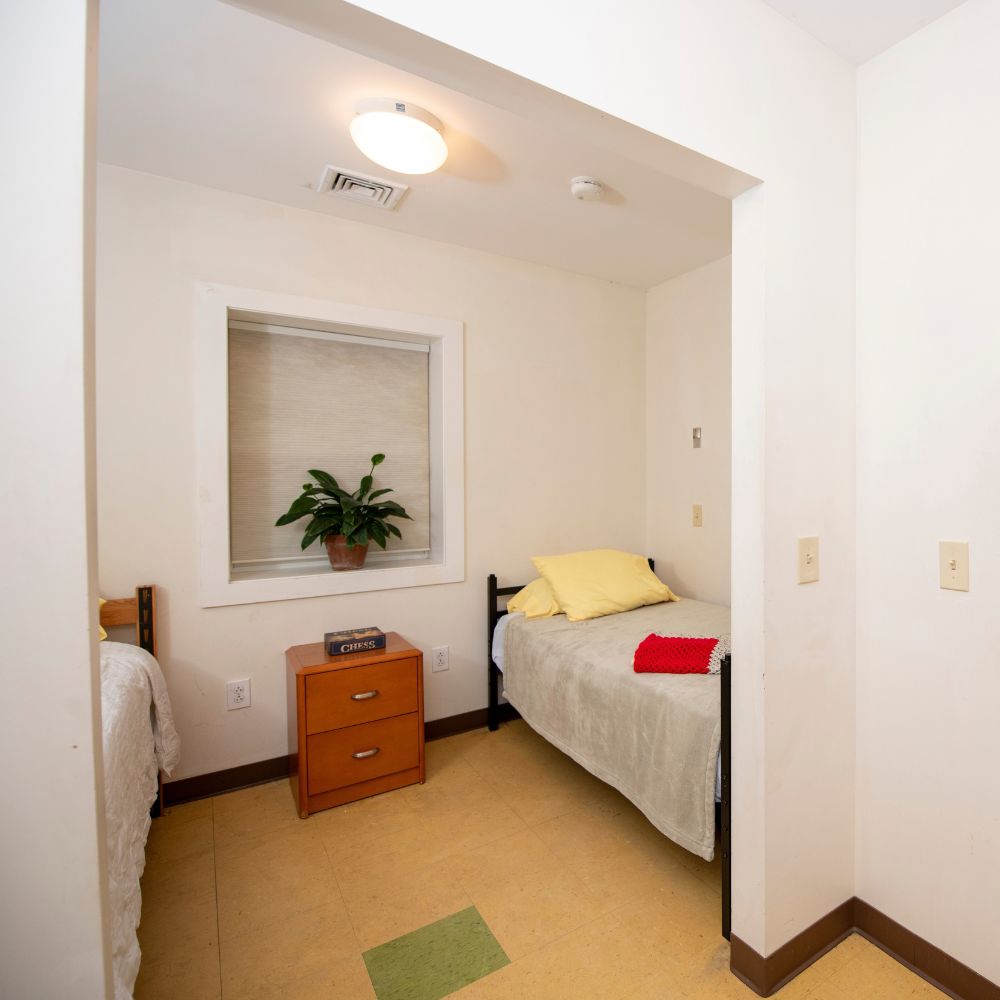 bedroom in hixon shelter, with two beds, a side table, and a plant in the window.